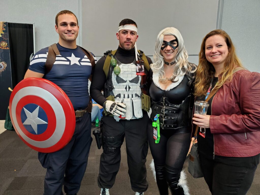 Four cosplayers dressed as Captain America, The Punisher, Black Cat, and Scarlet Witch at an indoor convention.