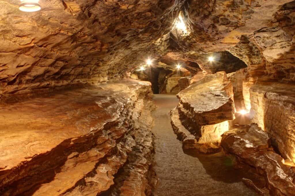 Interior walkway of Mark Twain Cave in Hannibal, Missouri, showing layered rock formations and warm ceiling lights illuminating the narrow cavern path.